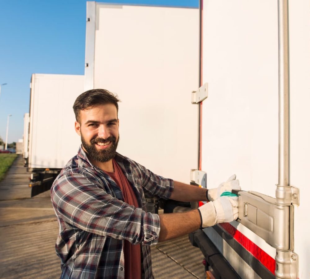 smiling-truck-driver-working-gloves-opening-closing-truck-trailer-back-doors-checking-goods-transportation (1)